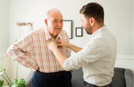 A caregiver helping an older man button his shirt at home