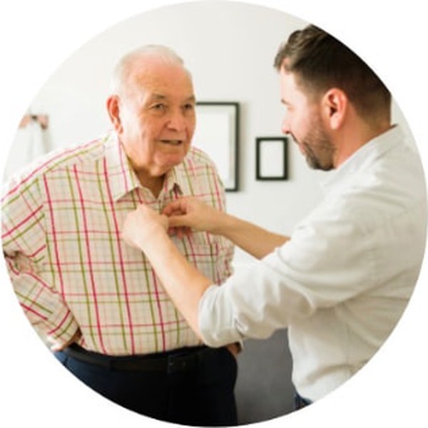 A caregiver helping an older man button his shirt at home