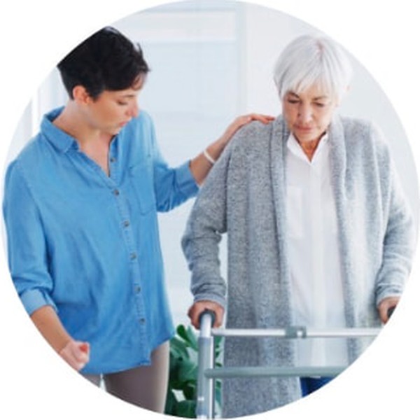 A caregiver helping an older woman walk with a rolling walker
